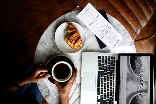 Top view of a marble table with coffee, croissant, and laptop perfect for a productive morning.